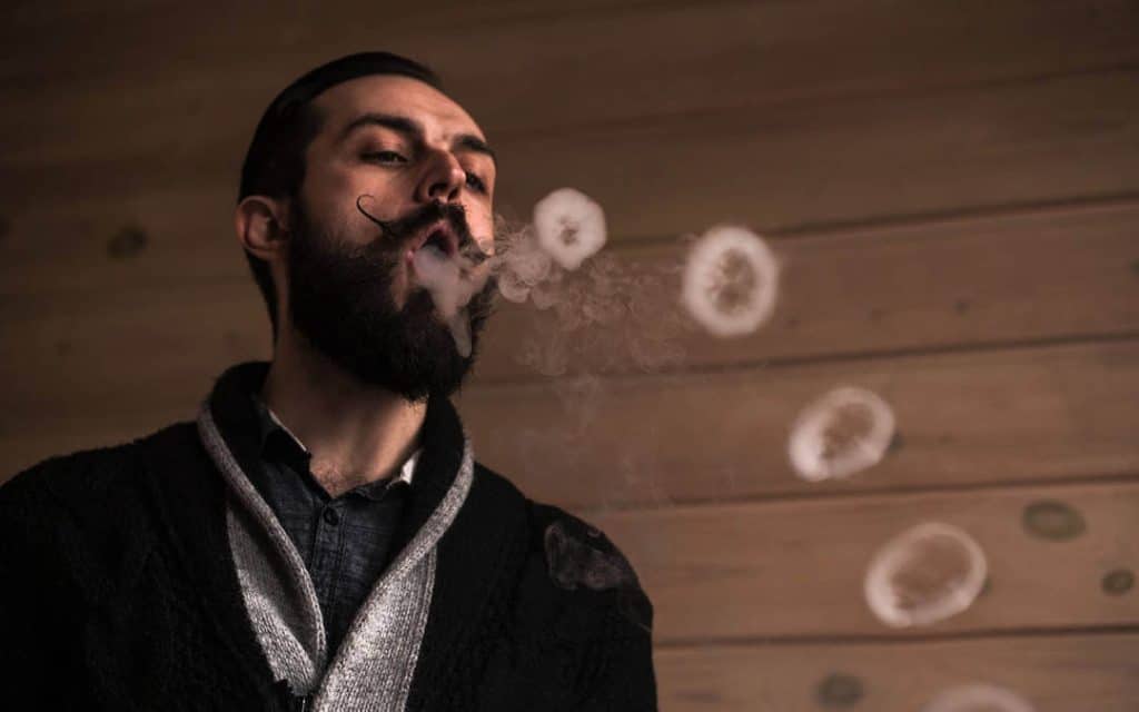 Homem de barba fazendo anéis de fumaça